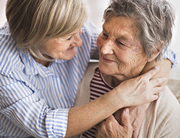 Two women with graying hair embrace and smile at each other. 