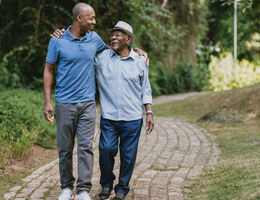 A middle-aged man and an older man walk on a path, talking and smiling.