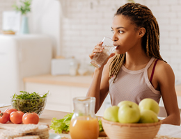 A woman drinks a glass of water at her kitchen counter