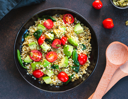 A bowl of brown rice with spinach, tomatoes, avocados and pumpkin seeds.