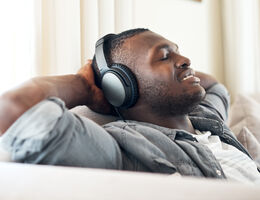 A man wearing over-ear headphones leans back on a couch, eyes closed.